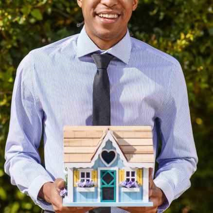 man in dress shirt holding a miniature wooden house